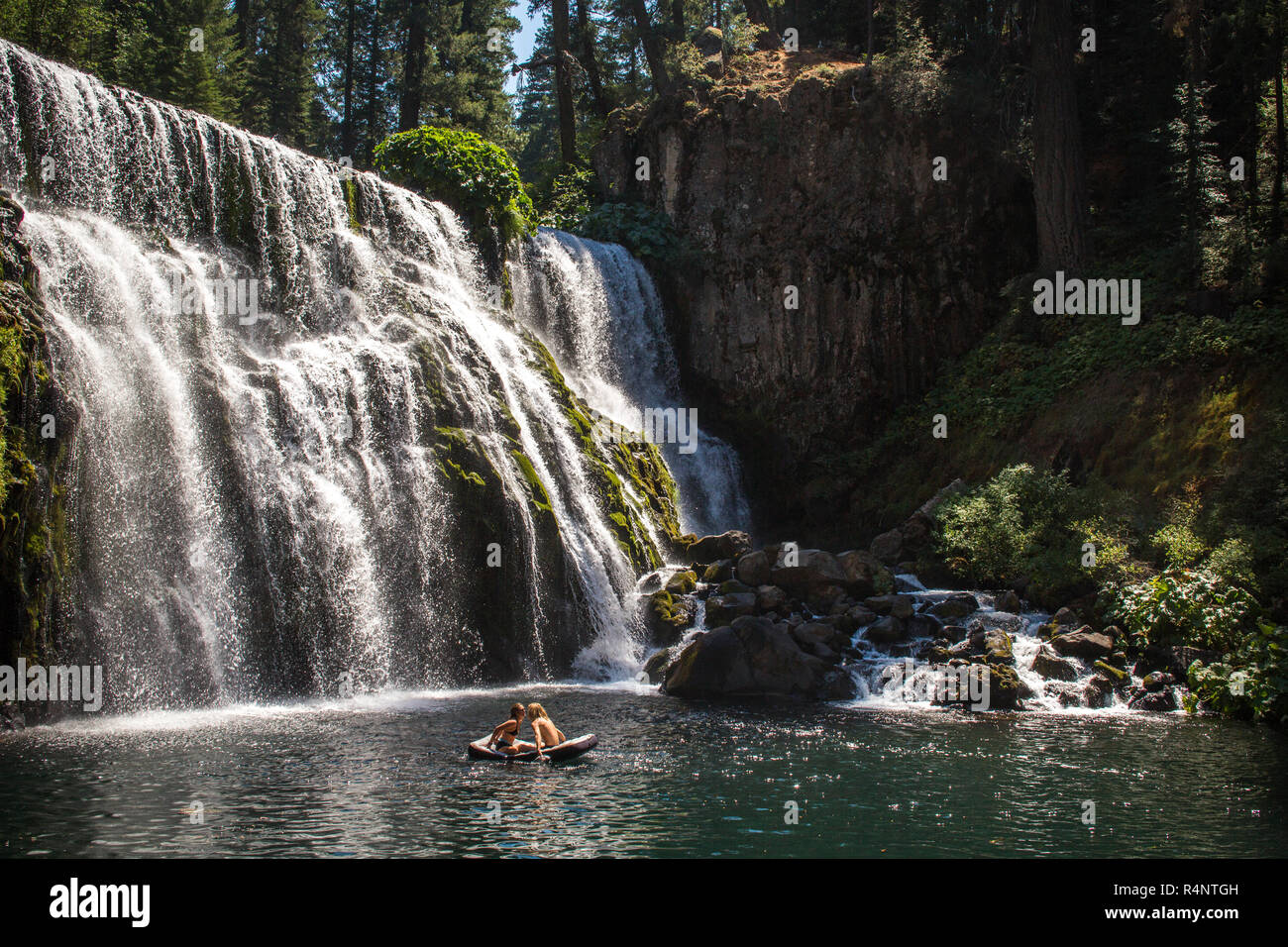 Distant view of couple in raft floating on water near waterfall, Â McCloudÂ River, California, USA Stock Photo