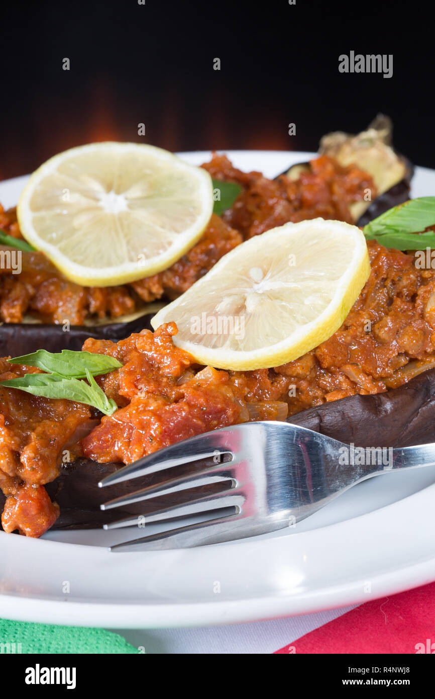A Turkish dish of Imam bayildi, baked egg plant/aubergine with a minced lamb and tomato topping served with fresh lemon slice garnish Stock Photo