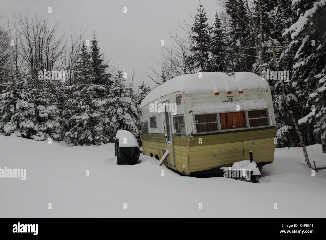 An old camper trailer covered in snow in the woods Stock Photo
