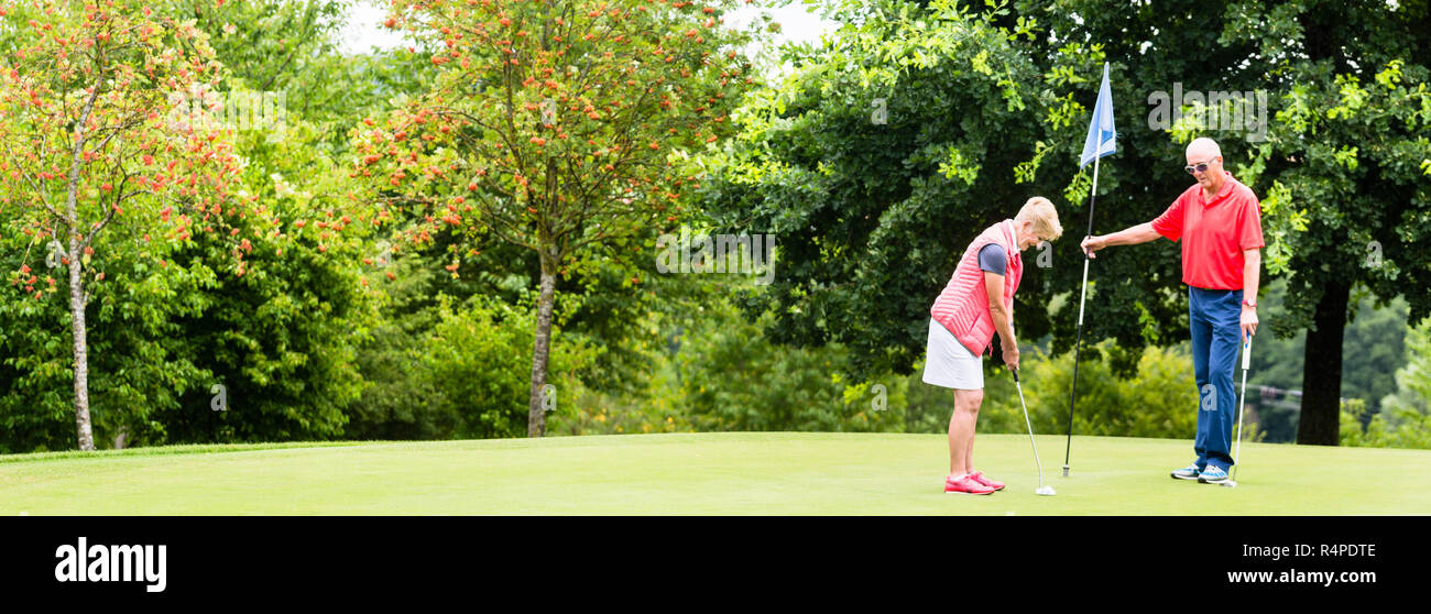 Senior woman and man playing golf putting on green Stock Photo