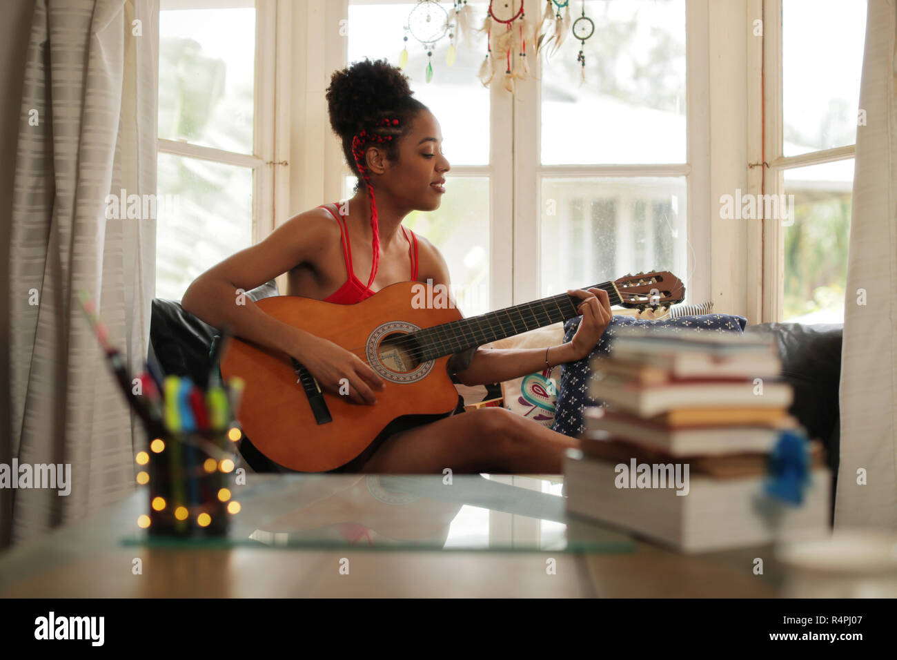 Mixed Race Girl Singing And Playing Classic Guitar At Home Stock Photo