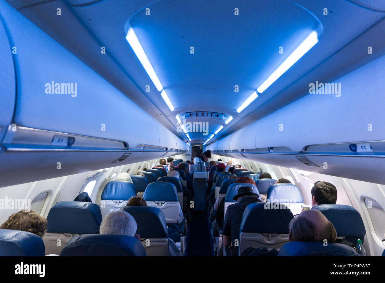 Interior of airplane full of seated passengers while in flight with EXIT sign clearly visible Stock Photo