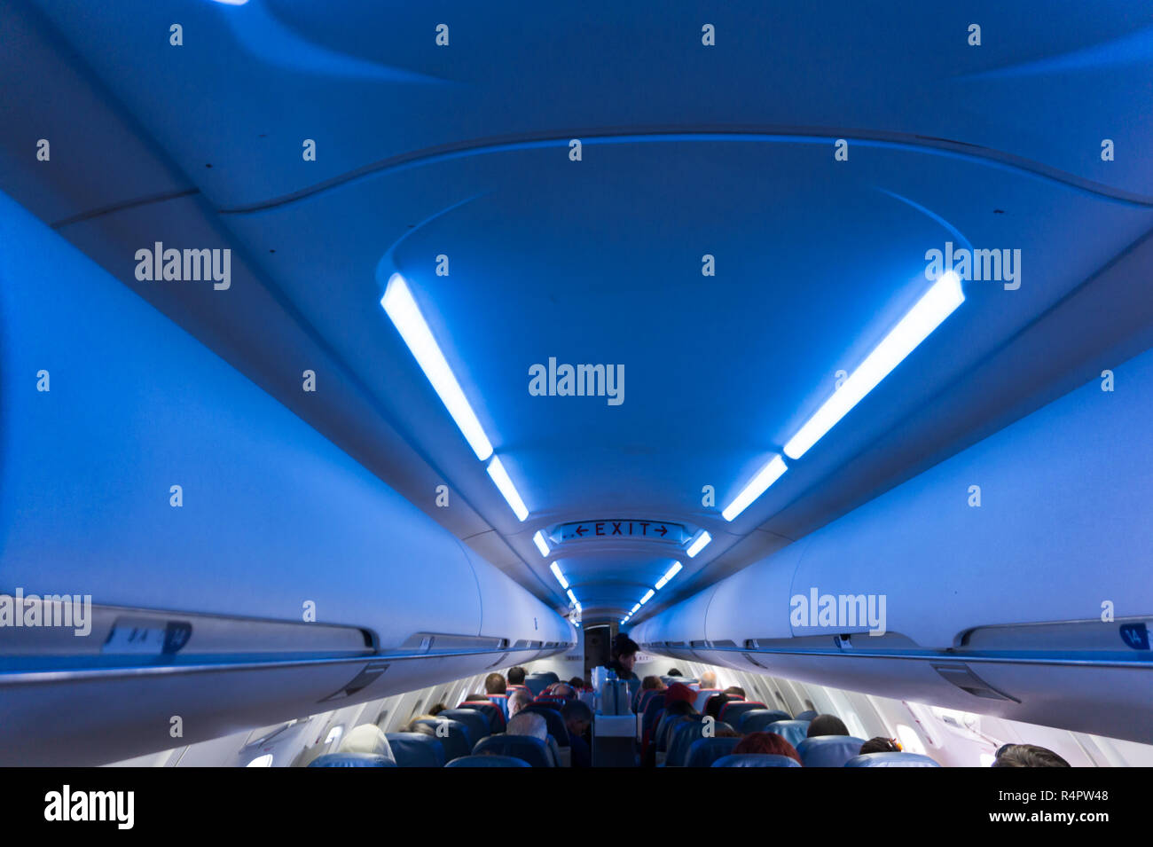 Interior of airplane full of seated passengers while in flight with EXIT sign clearly visible Stock Photo