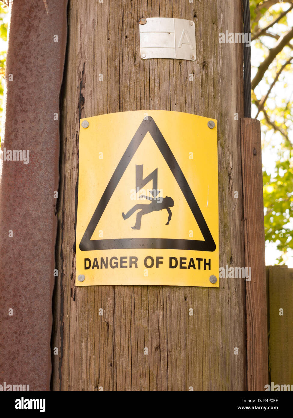 a yellow and black danger of death sign with triangle and lightening bolt on a wooden electric pole pylon Stock Photo