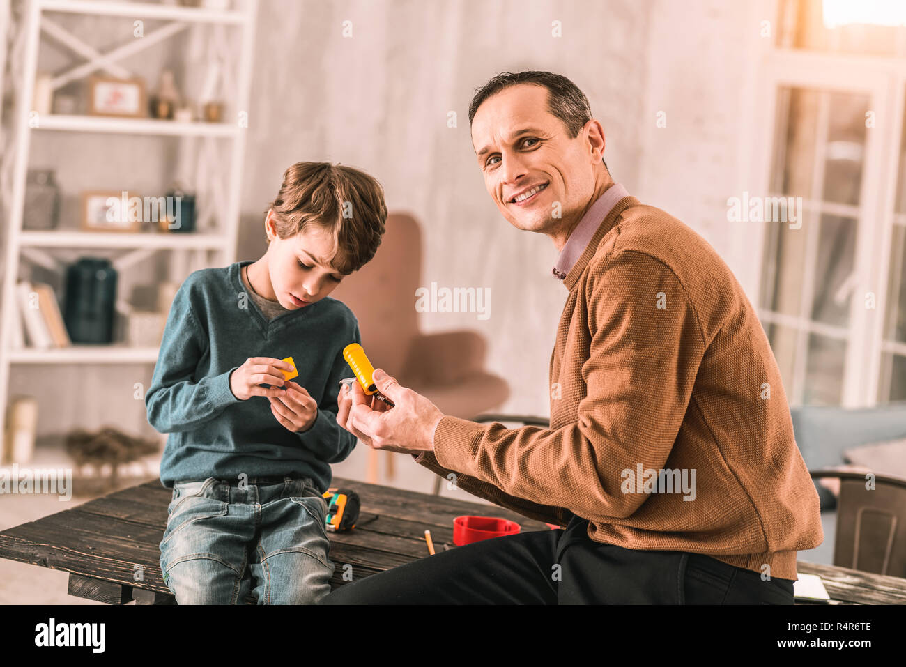 Father proudly smiling at the camera while working on a project with his son. Stock Photo
