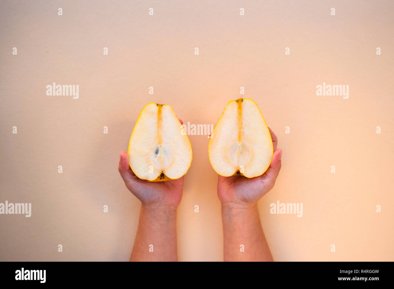 Two yellow sweet and ripe pears in hchild's hands on a beige background. Minimal food concept. Stock Photo