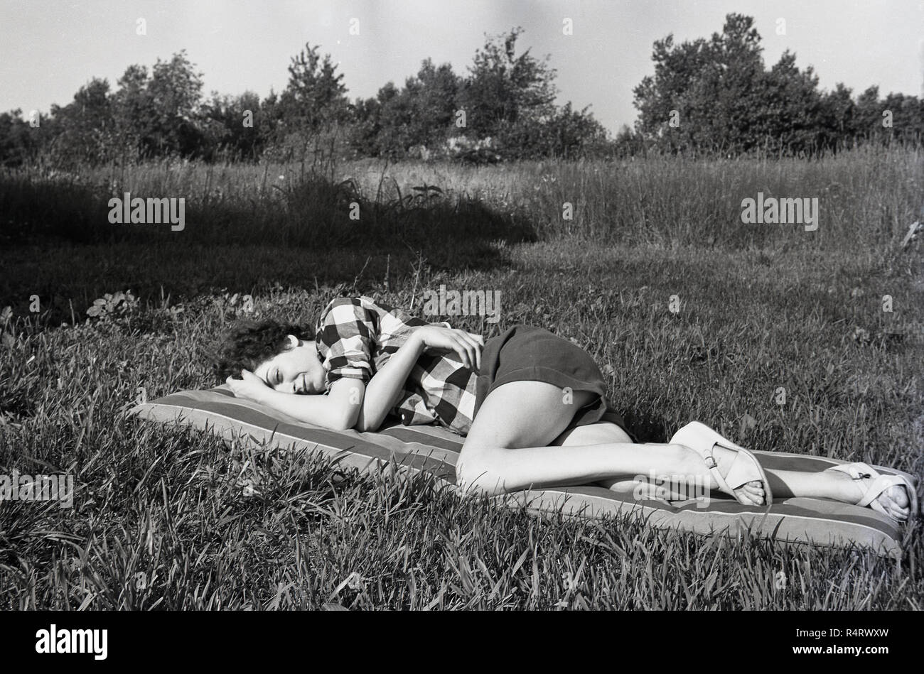 1960s, historical, summertime and outside in a grassy field, a lady lying down on an air bed or lylo relaxing, England, UK. Stock Photo
