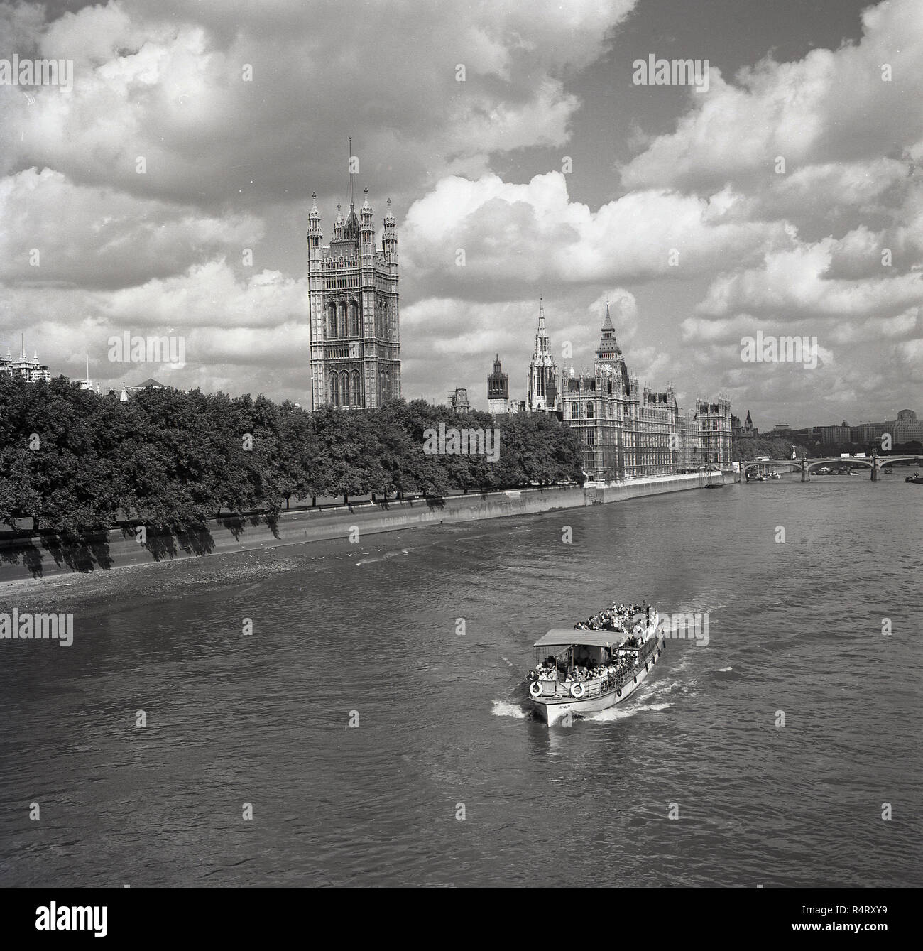 1960s, historical, summertime and a pleasure boat going down the river Thames having just past the Houses of Parliament, the buildings of the government of the UK, London, England, UK. Stock Photo