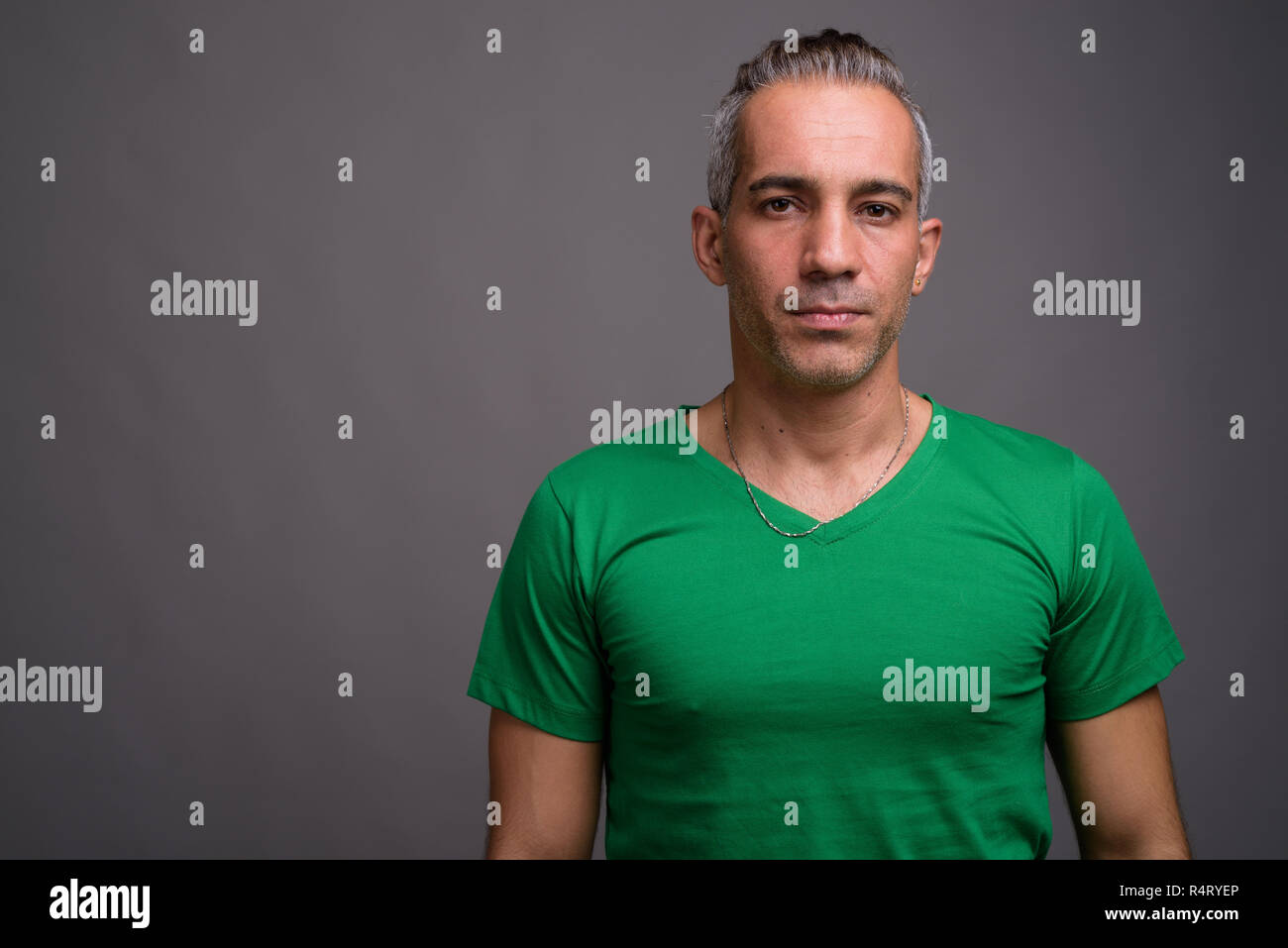 Handsome Persian man with gray hair wearing green t-shirt Stock Photo