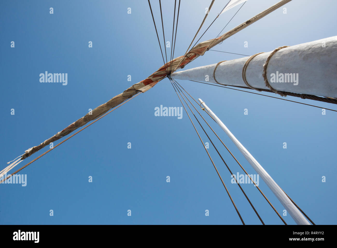 Abstract view of wooden sailing boat mast with rigging and blue sky background Stock Photo