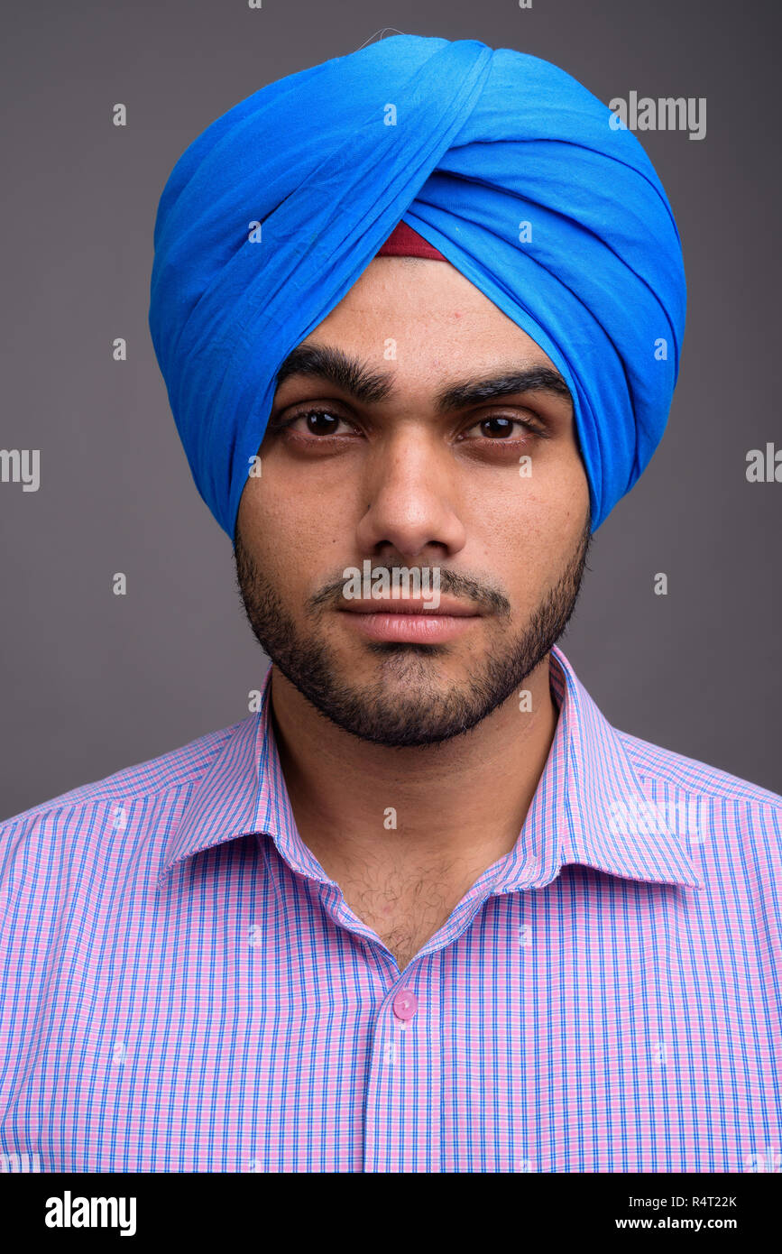 Young handsome Indian businessman wearing turban against gray ba Stock Photo