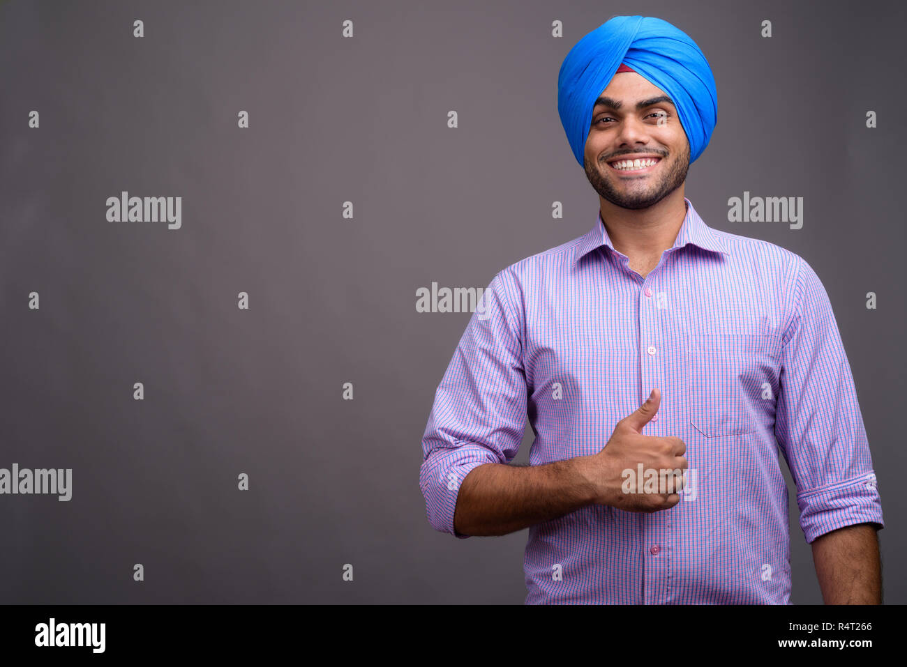 Young handsome Indian businessman wearing turban against gray ba Stock Photo