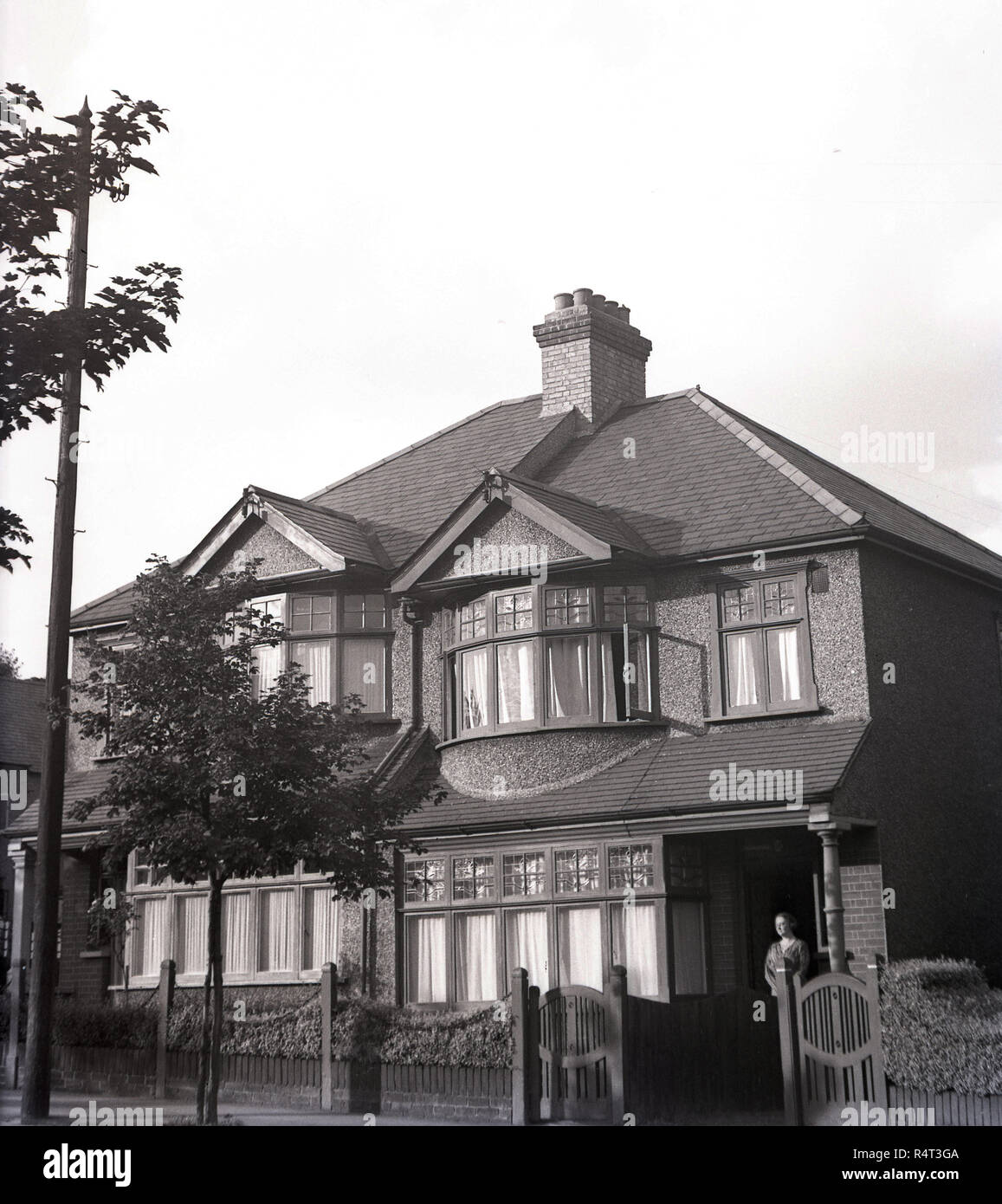 1940s, historical, a lady standing at the entrance of a semi-detached two-storey house suburban house, England, UK. Built in the 1920s, the house had wooden box casement windows and a pebble dash exterior. Stock Photo