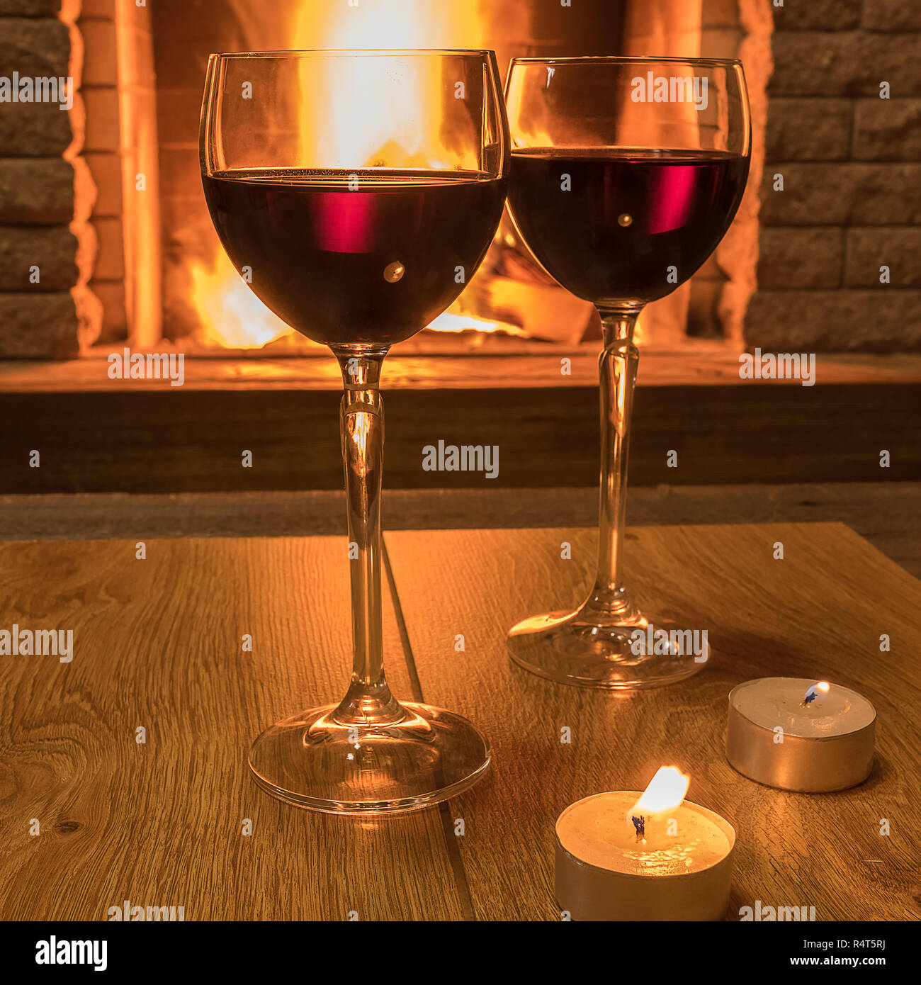 tranquil scene before cozy fireplace, with two glasses of red wine and candles, in country house, in winter vacation. Stock Photo