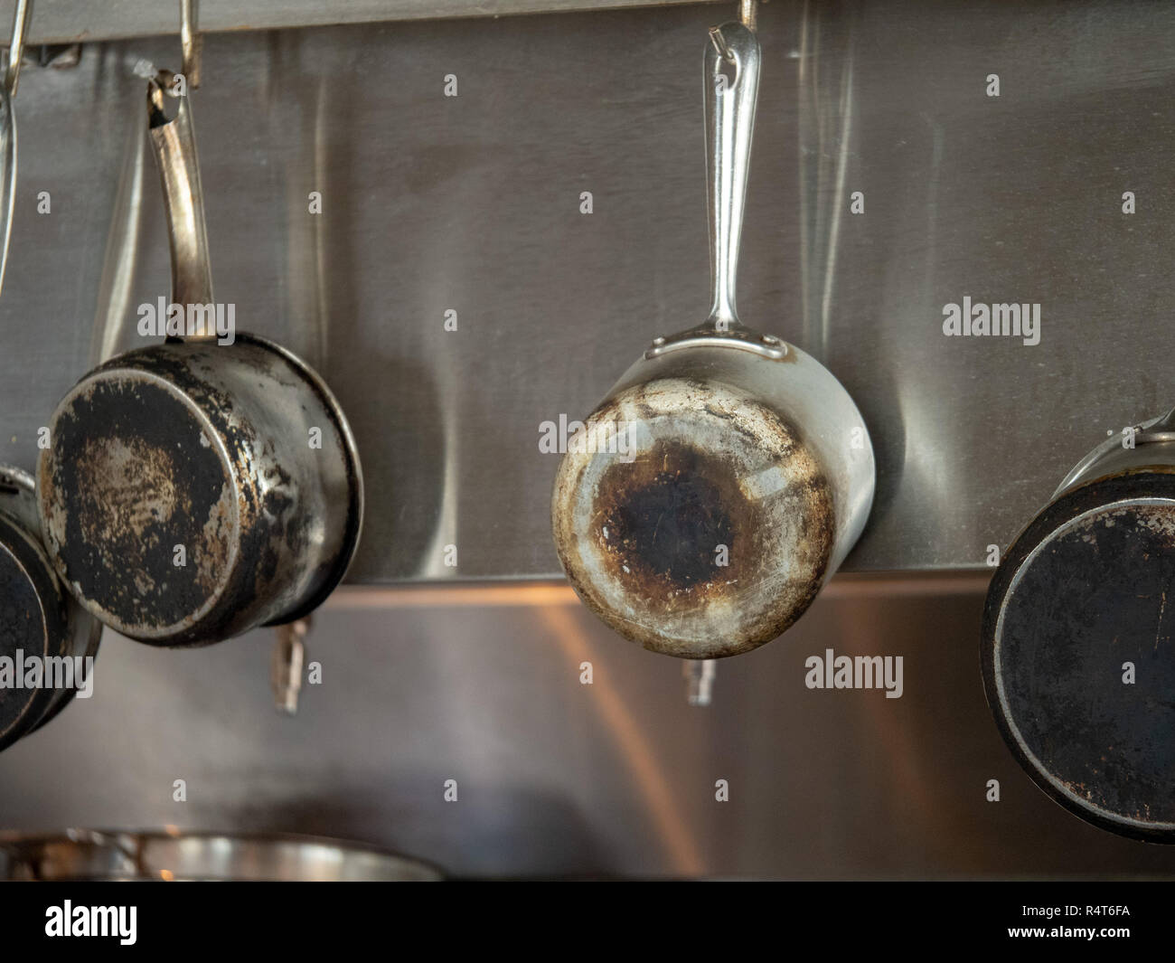Four steel saucepans with burnt bottoms hanging in industrial kitchen