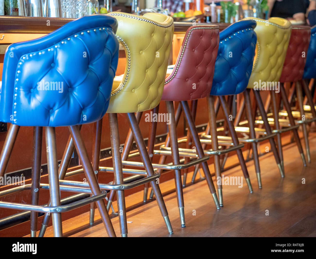Blue, yellow, and red leather bar chairs lined up in front of bar