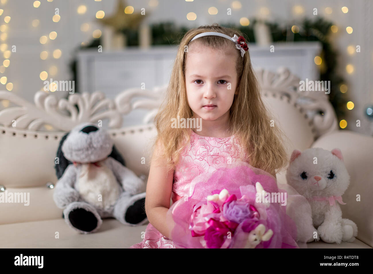 A girl in a pink dress with fair blond hair on a white ottoman Stock Photo