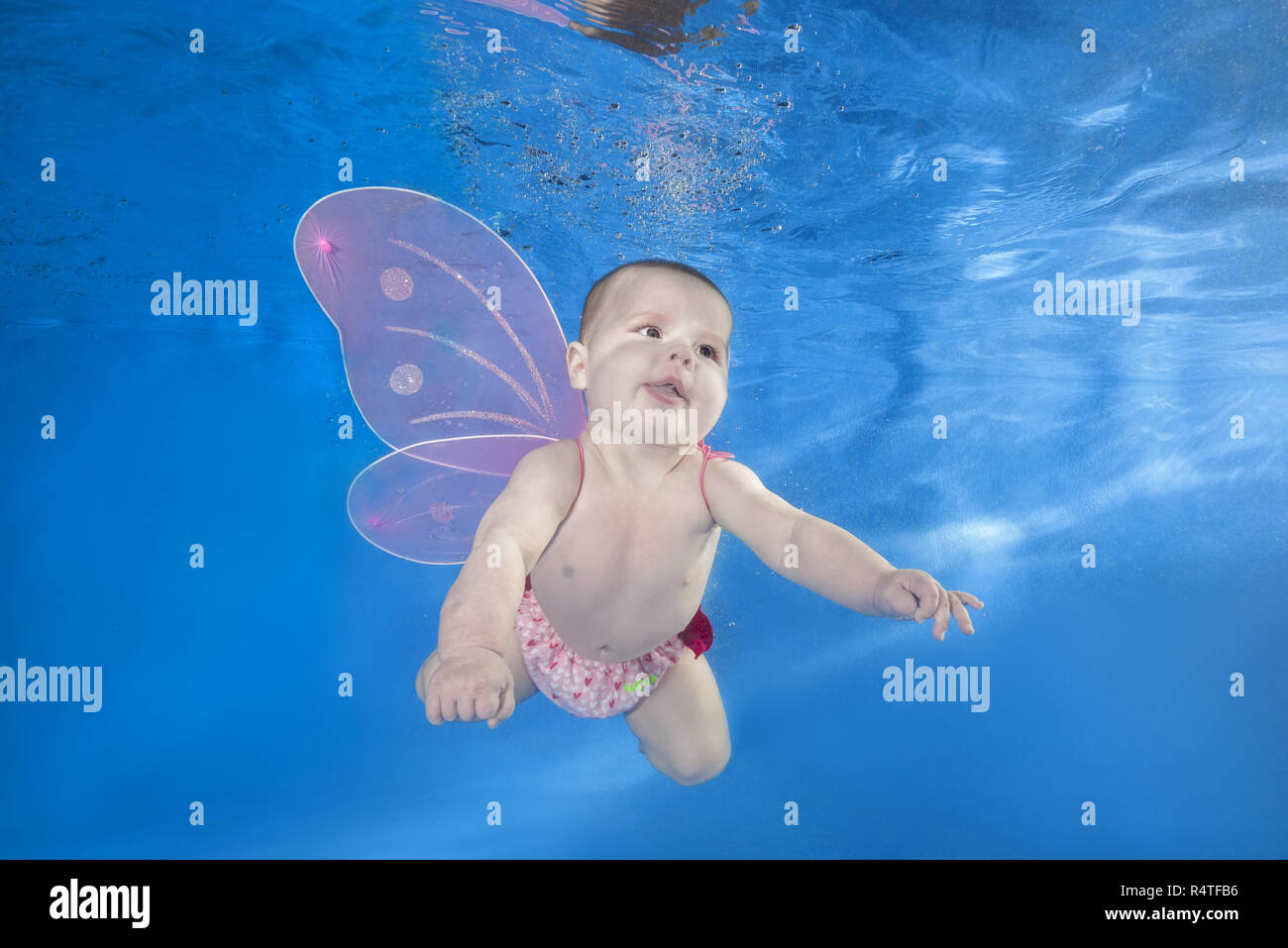 Baby girl in fairy costume swim underwater on blue water background. Healthy family lifestyle ...