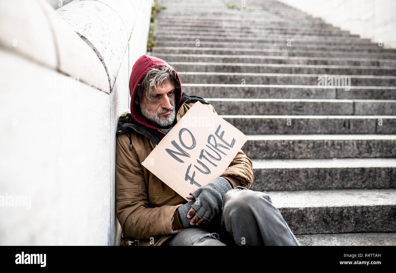 Homeless beggar man sitting on stairs outdoors in city holding no future cardboard sign. Stock Photo