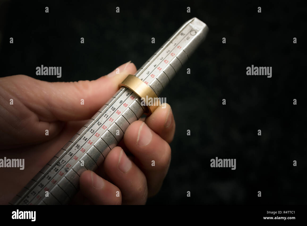 hand of a goldsmith measures a golden ring on a sizer gauge, jeweler