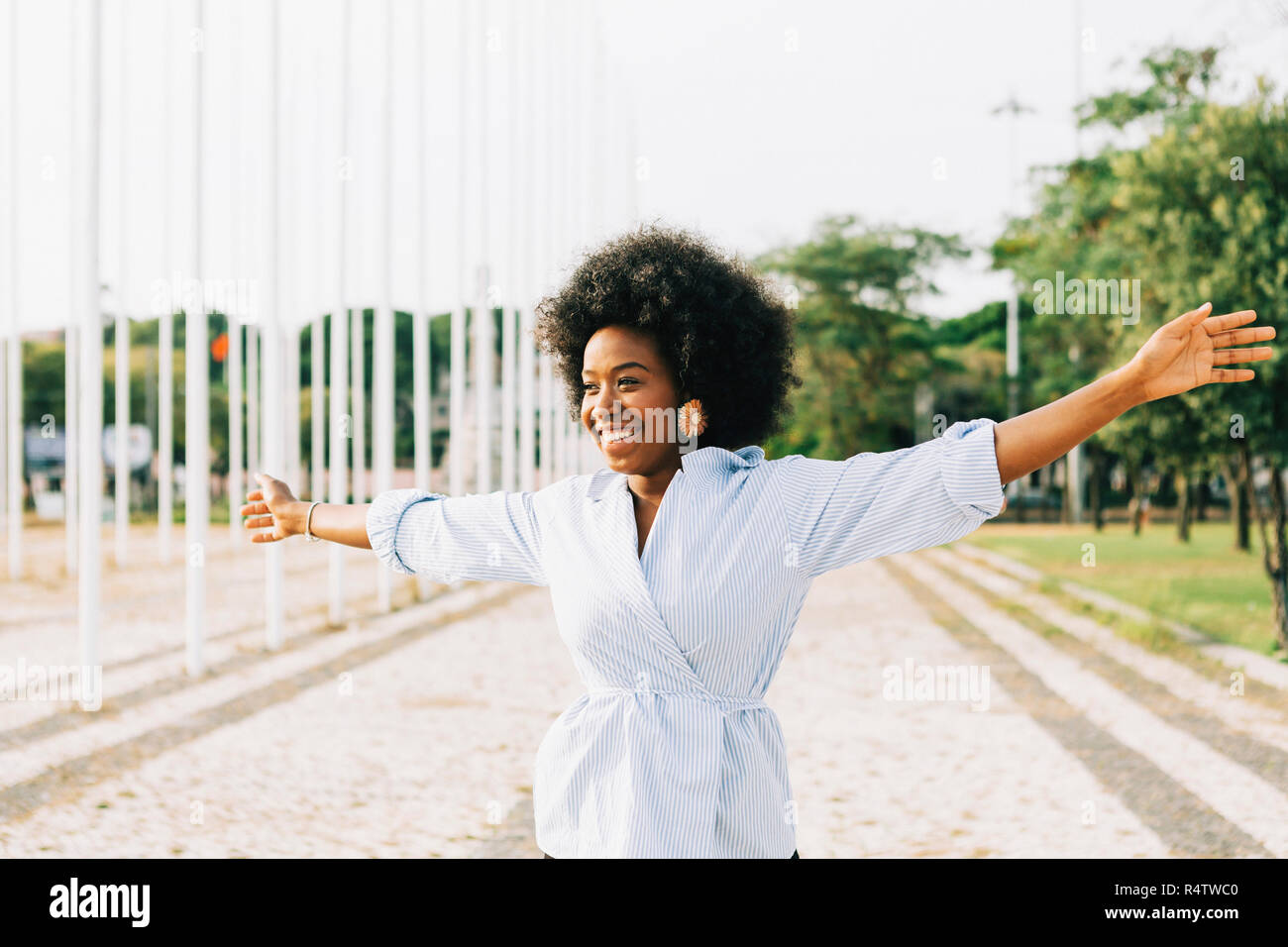 Carefree young woman with arms outstretched in sunny park Stock Photo