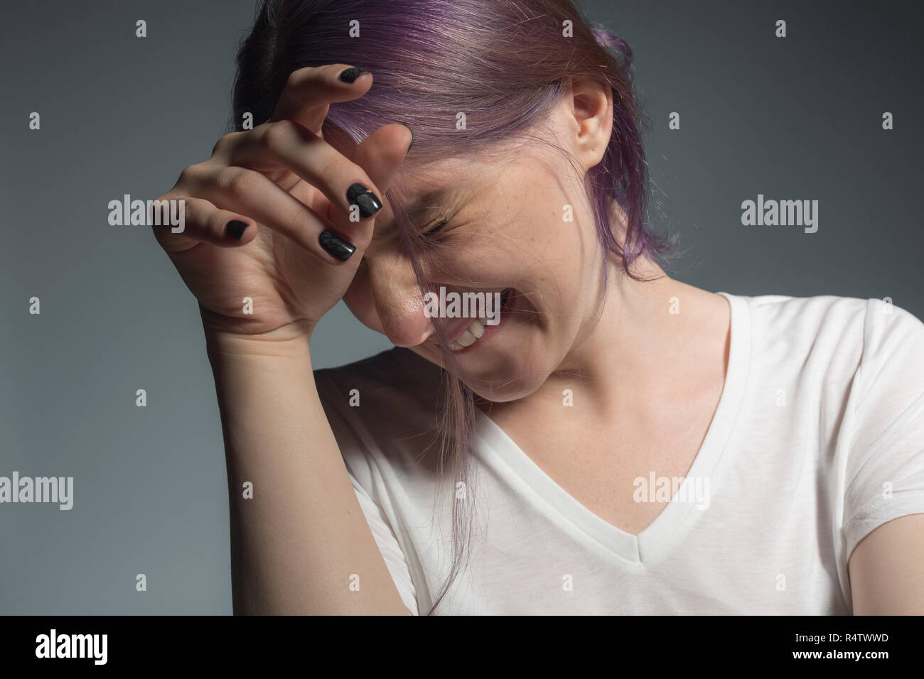 Young woman with dyed hair looking away and wincing against gray background Stock Photo