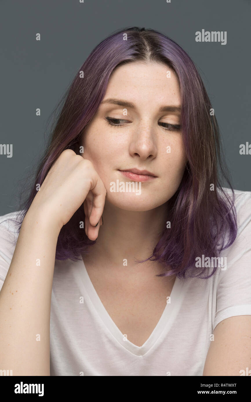 Portrait of a young woman with dyed hair and looking down against gray background Stock Photo