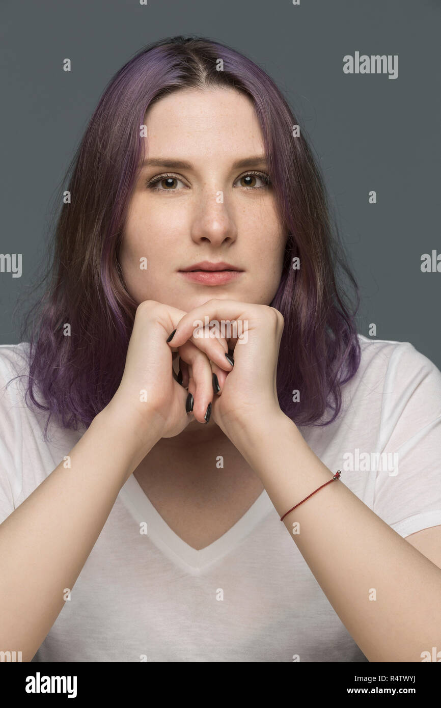 Portrait of a young woman with dyed hair and resting chin on hands against gray background Stock Photo