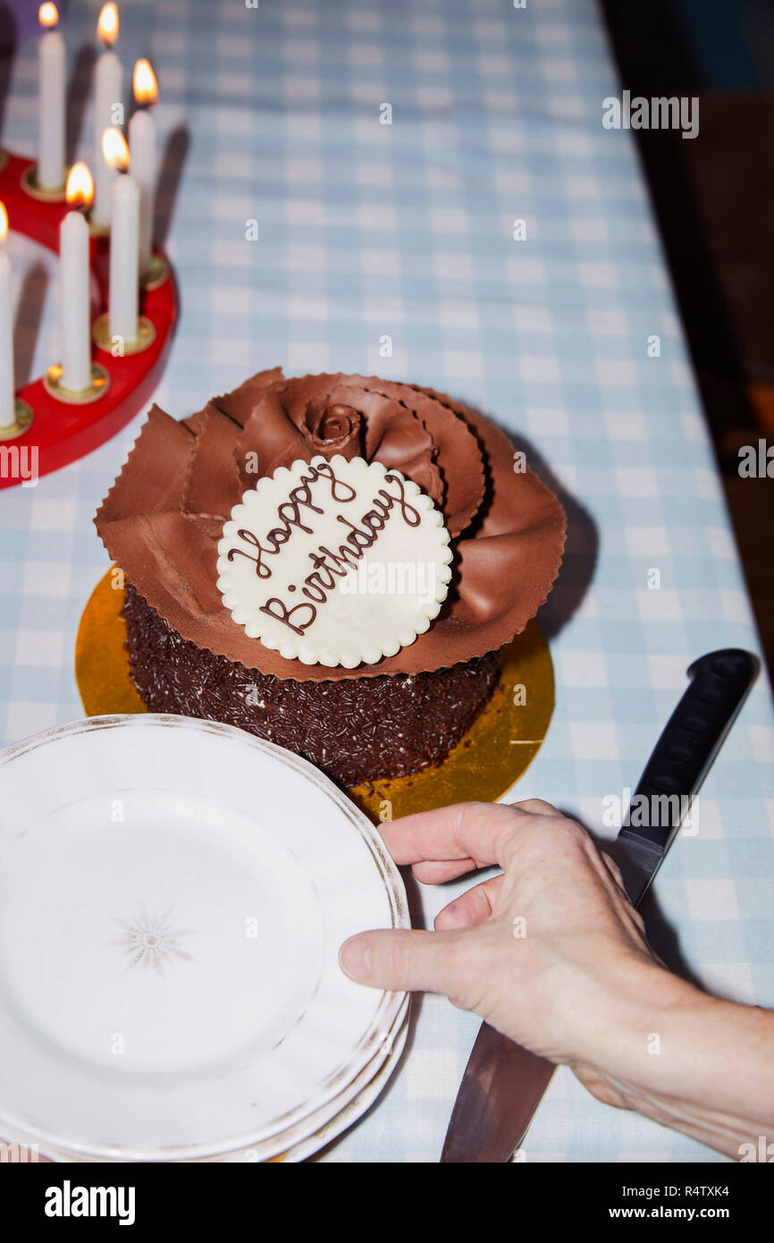 Woman reaching for plate next to chocolate birthday cake Stock Photo