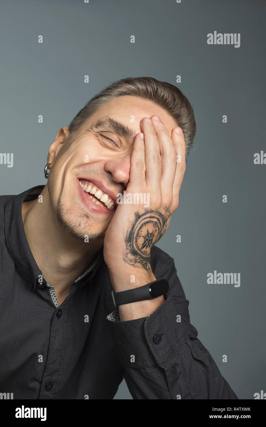 Portrait of man smiling with head in hands against gray background Stock Photo