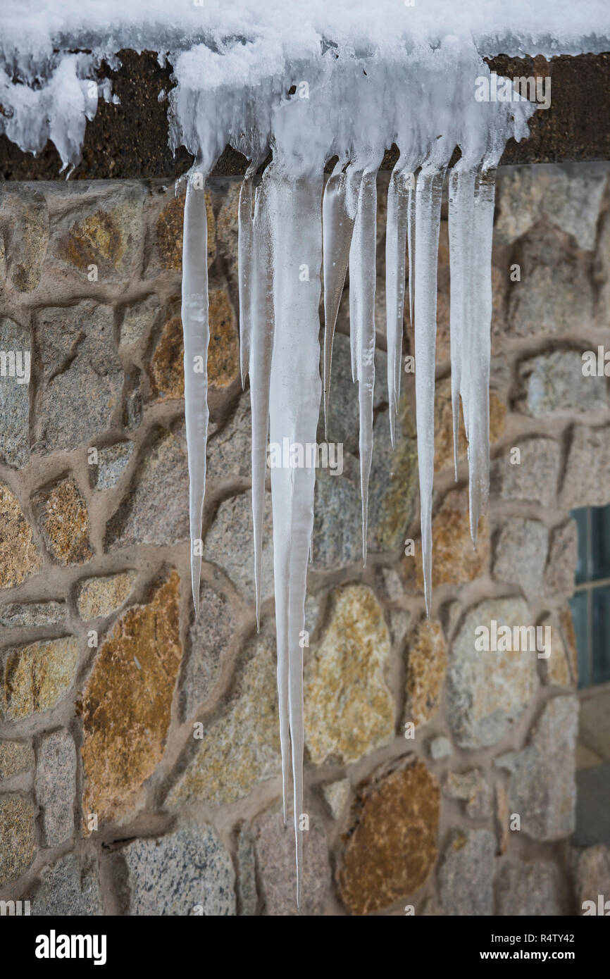 Icicles hanging over stone house roof Stock Photo