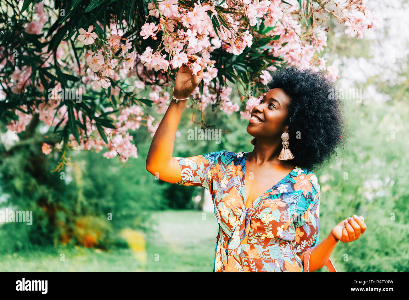 Young woman standing below tree with pink blossoms Stock Photo