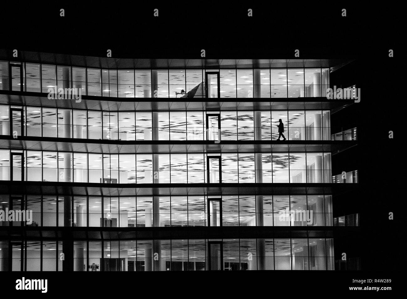 A lone figure walks along the balcony of an empty office building at night in Bristol in the united Kingdom. Stock Photo