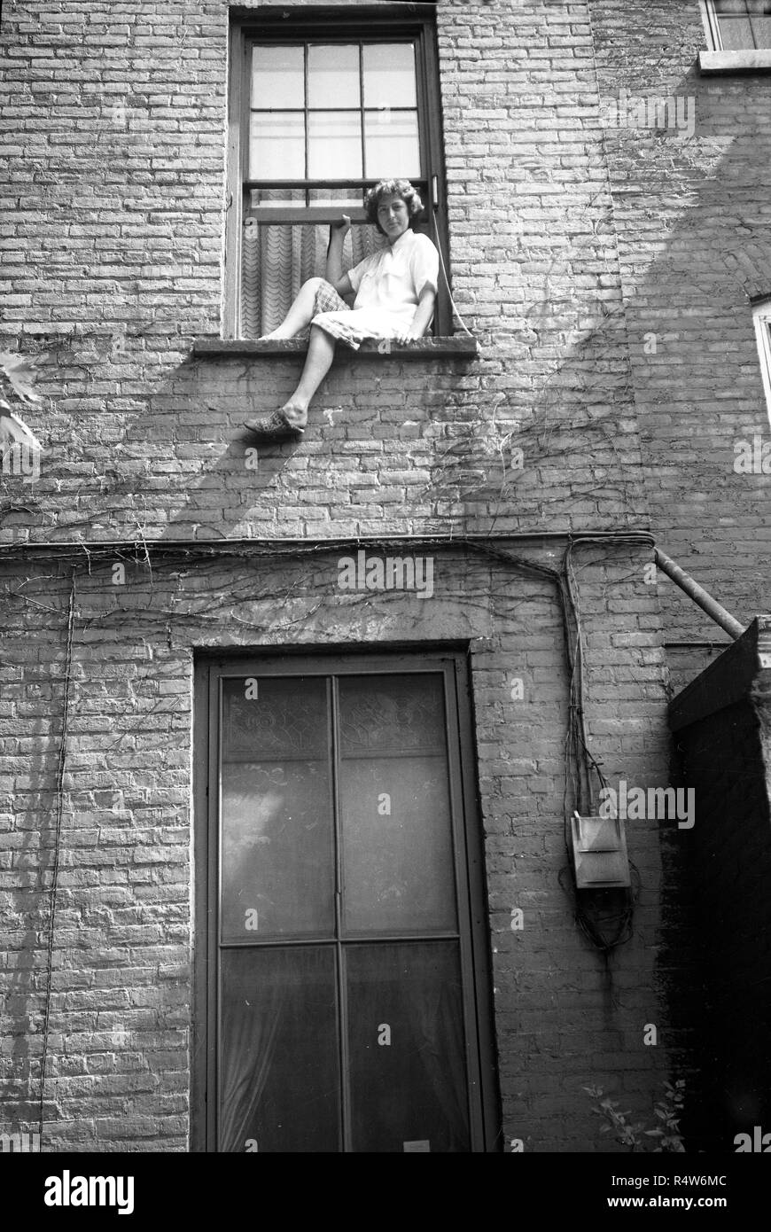 Young woman sitting on tenement window ledge in the Bronx,  New York USA 1945 Stock Photo