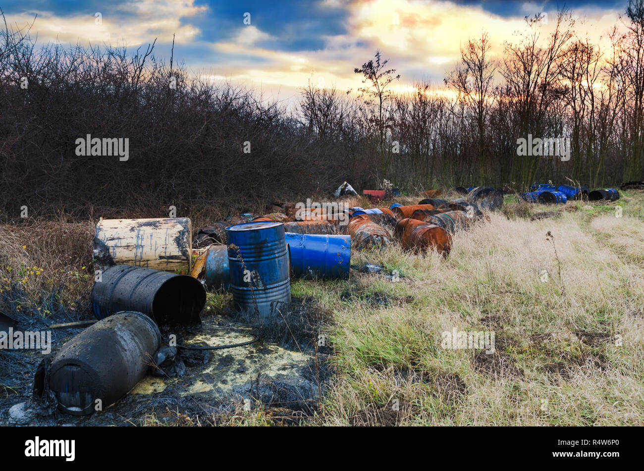 Barrels of toxic waste in nature with dramatic sunsets. Environmental pollution. Stock Photo