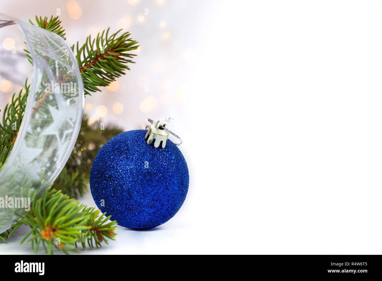 Blue glitter Christmas ball, branch of tree fir and silver ribbon on white background with copy space for text.Selective focus. Stock Photo