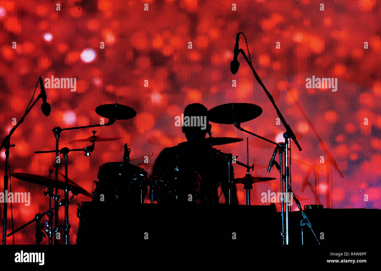 A silhouette of a drummer in a music concert against a red pattern screen behind. Stock Photo