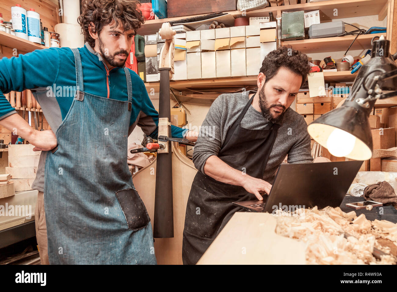 two craftsmen violinmakers checking data and measures for a new violin with computer Stock Photo