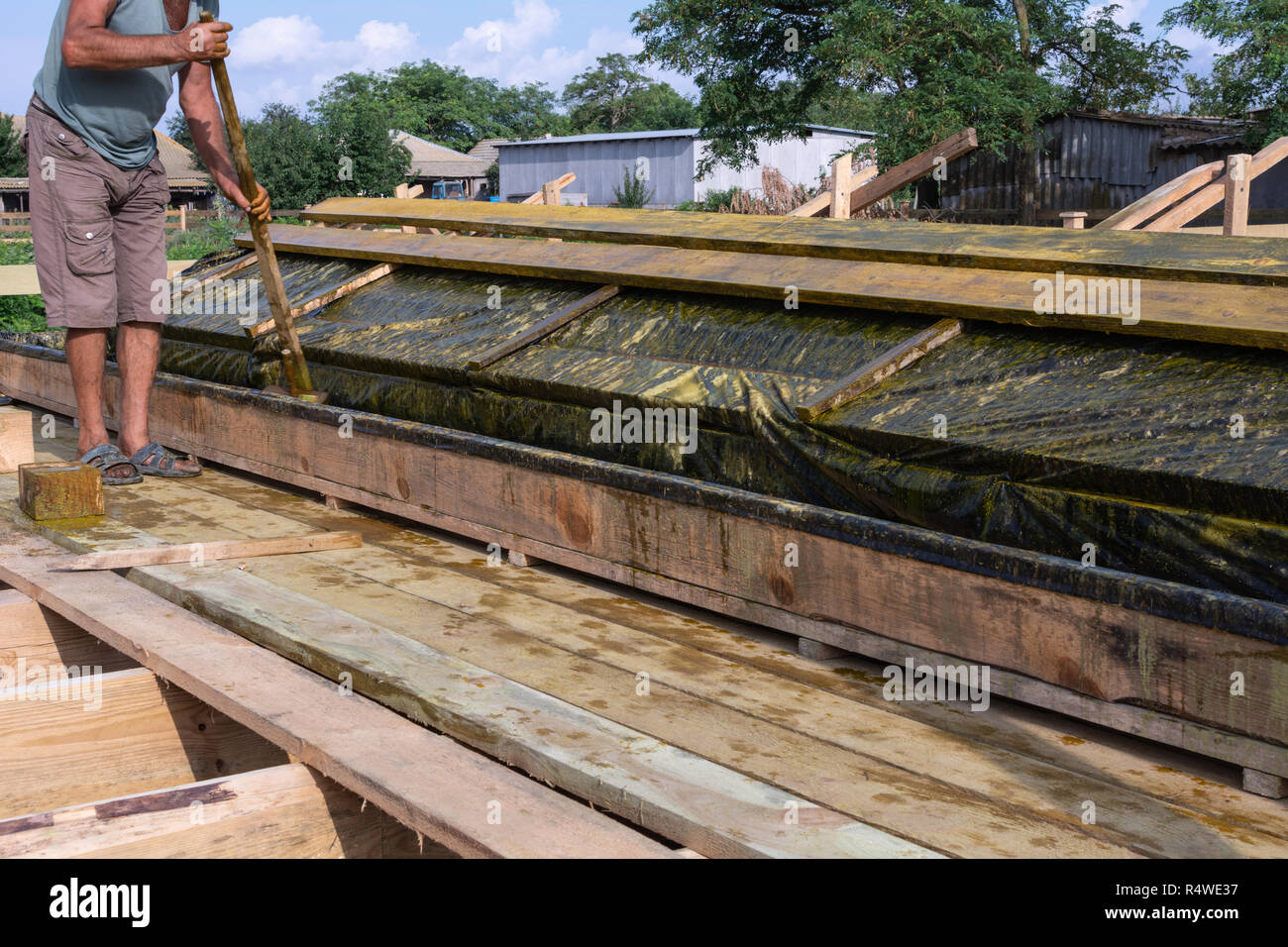 Worker at a construction site at home covers antiseptic boards. Impregnation of boards. Stock Photo