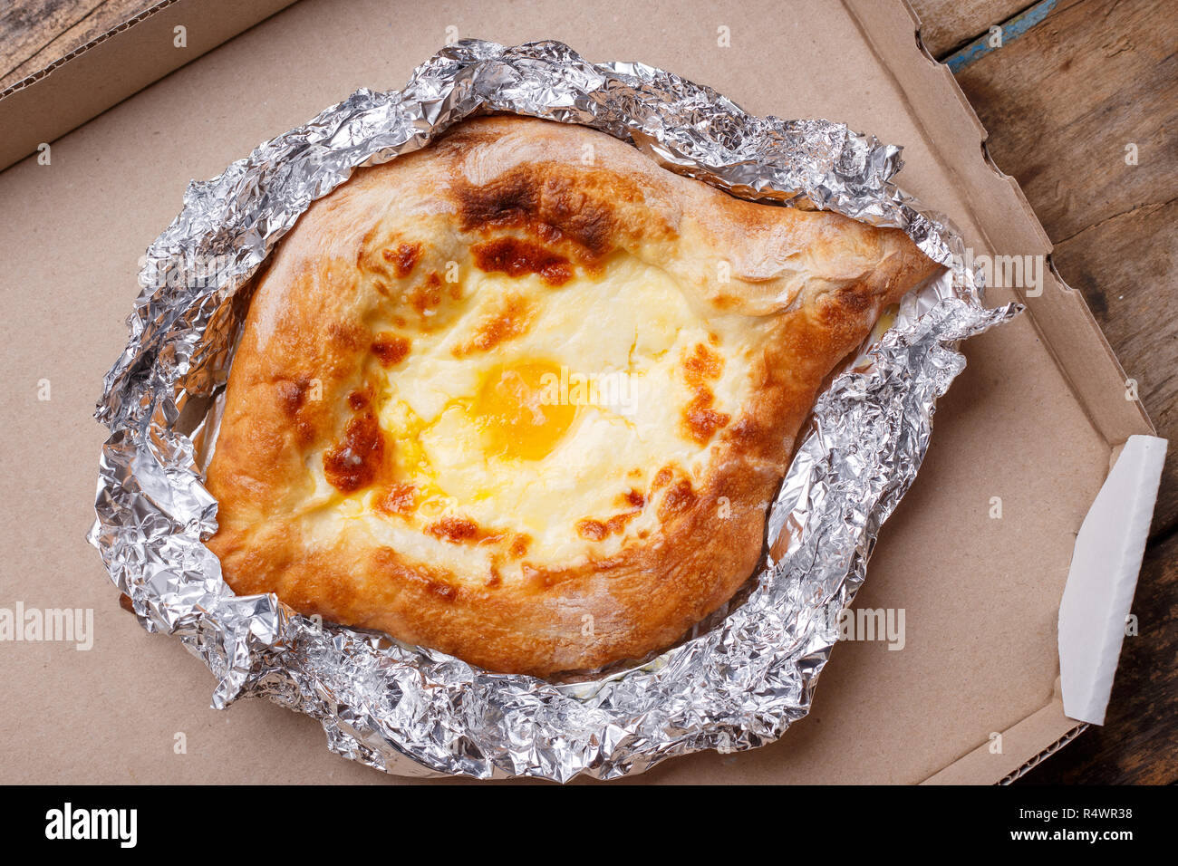 Adjarian open khachapuri with cheese and egg on wooden board. Traditional Caucasian take away and street food Stock Photo
