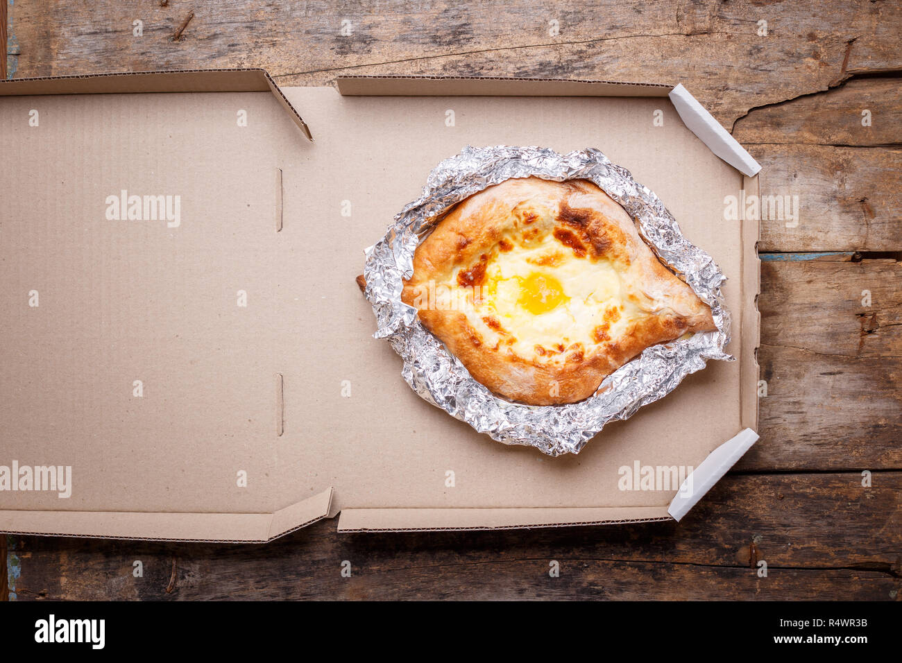 Adjarian open khachapuri with cheese and egg on wooden board. Traditional Caucasian take away and street food Stock Photo
