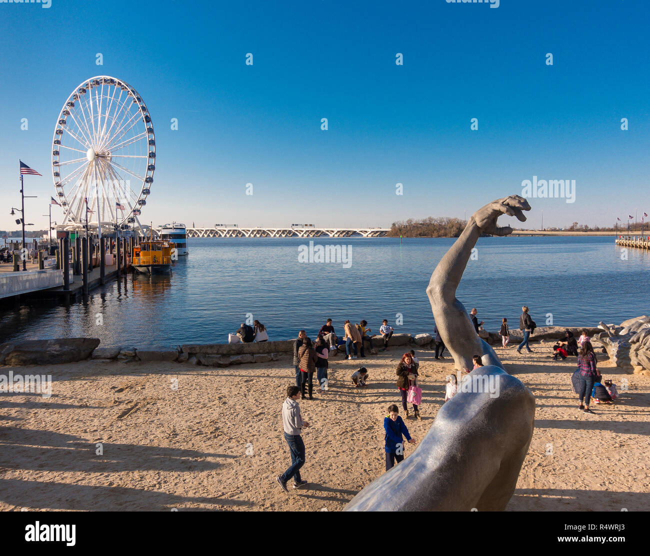 NATIONAL HARBOR, MARYLAND, USA - The Awakening sculpture and people on beach, with Capital Wheel amusement ride at left. Stock Photo