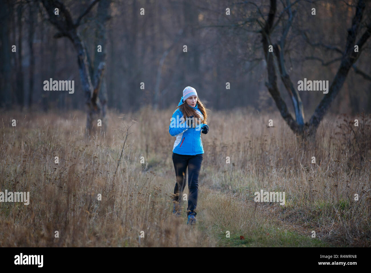 Young slim woman running in cold weather in late fall. Girl jogging in autumn park Stock Photo