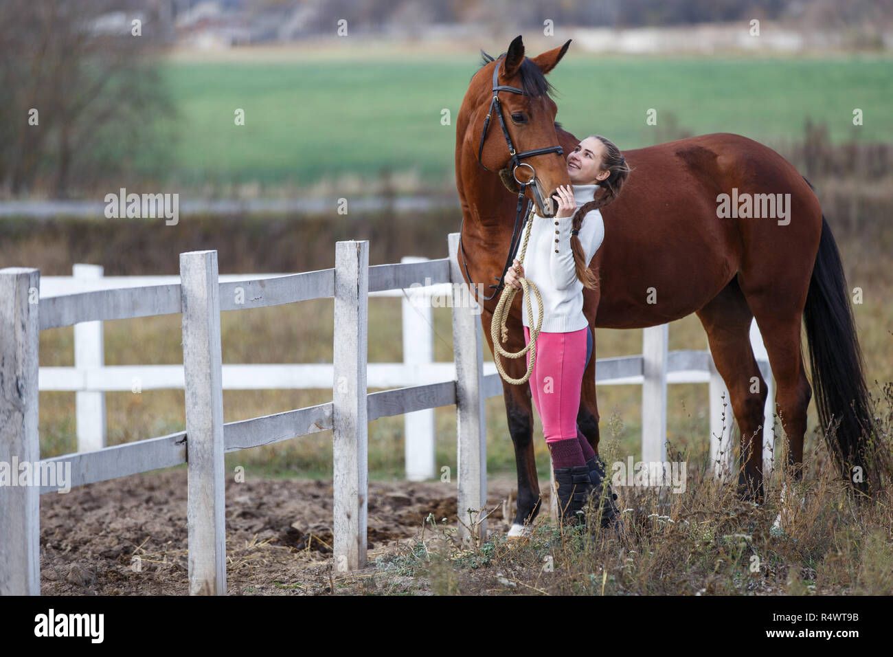 Young girl standing with her bay horse near paddock. Equestrian life concept background Stock Photo