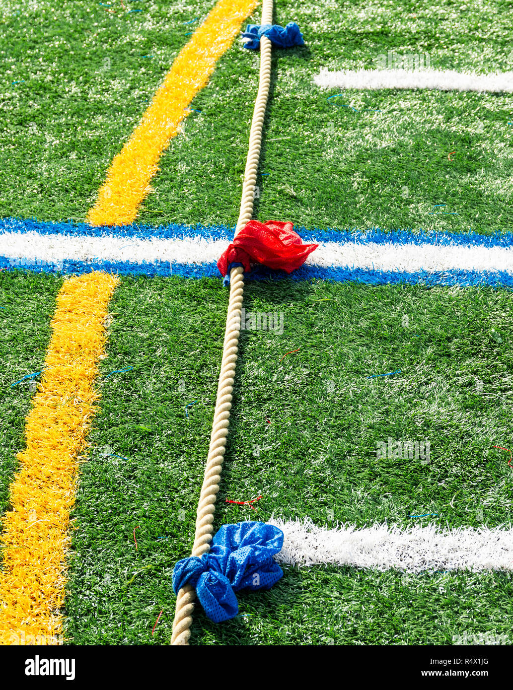 A tug of war rope with blue and red markers on it lying on a green