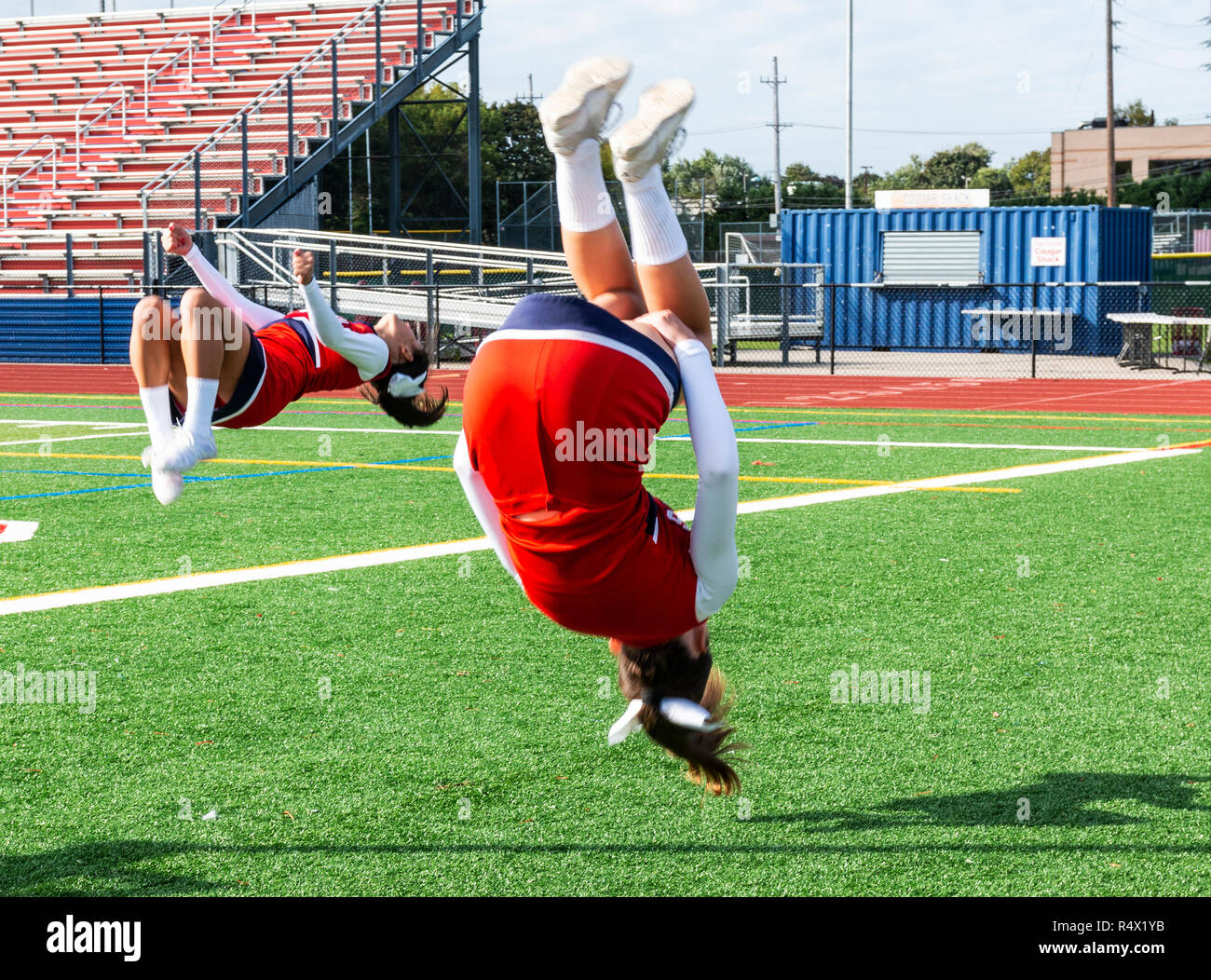 Two high school cheerleaders are practicing flips on the infield before a football game. Stock Photo