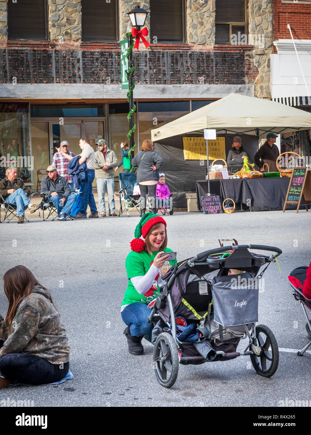 LINCOLNTON, NC, USA-11/25/18: Young mother smiles as she takes picture of her infant in a stroller, waiting for Christmas parade to start. Stock Photo