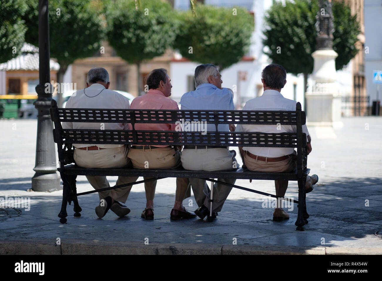 Four Spanish men sitting, talking, on a bench in a square. Stock Photo