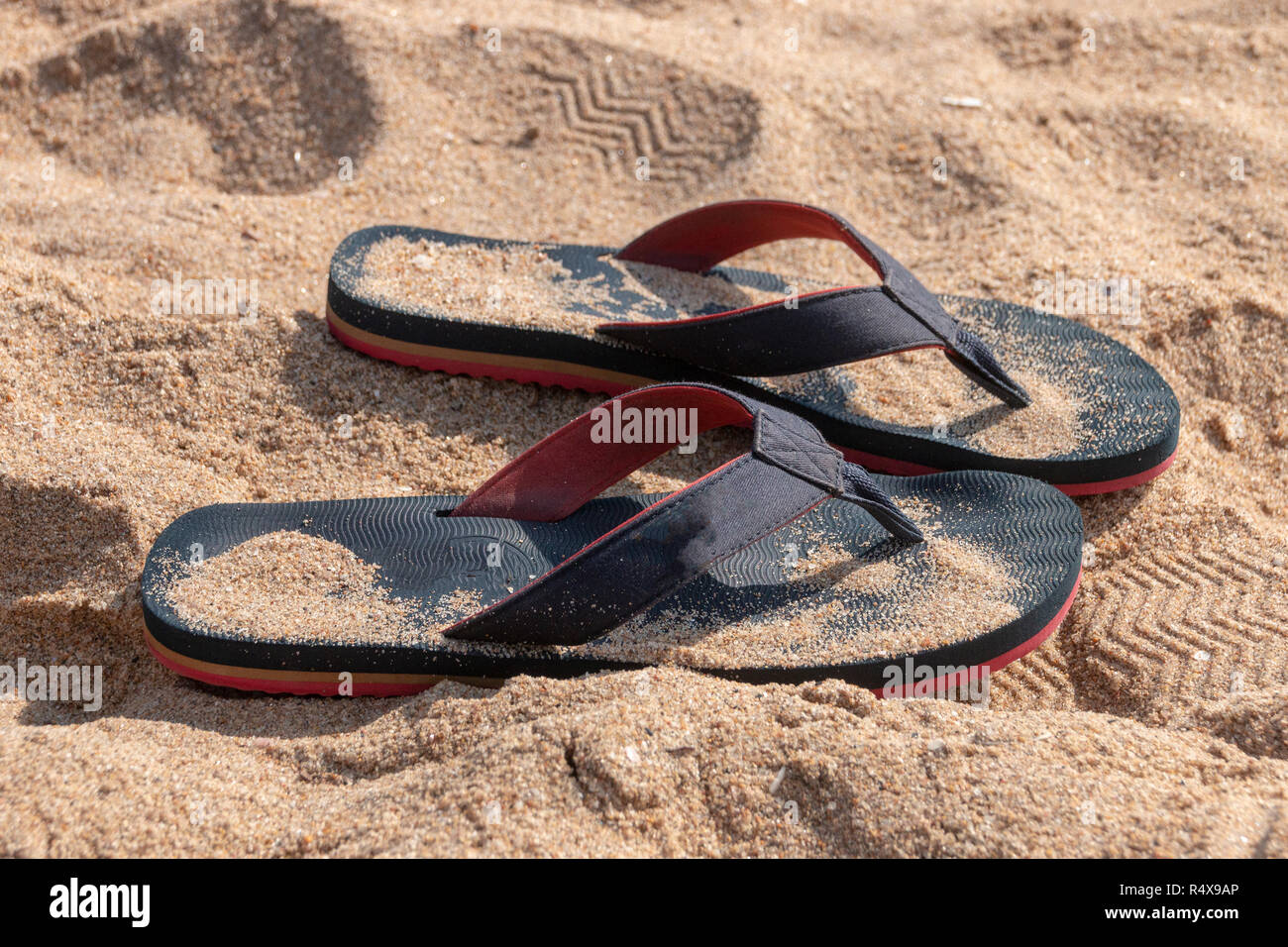 A Close up view of a pair of blue and red slops in the beach sand on a sunny summers day Stock Photo