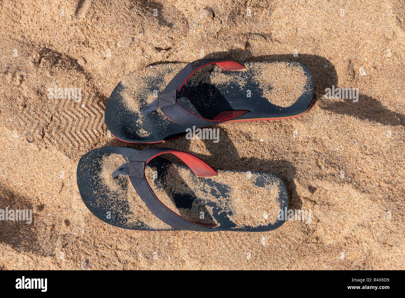 A Close up view of a pair of blue and red slops in the beach sand on a sunny summers day Stock Photo